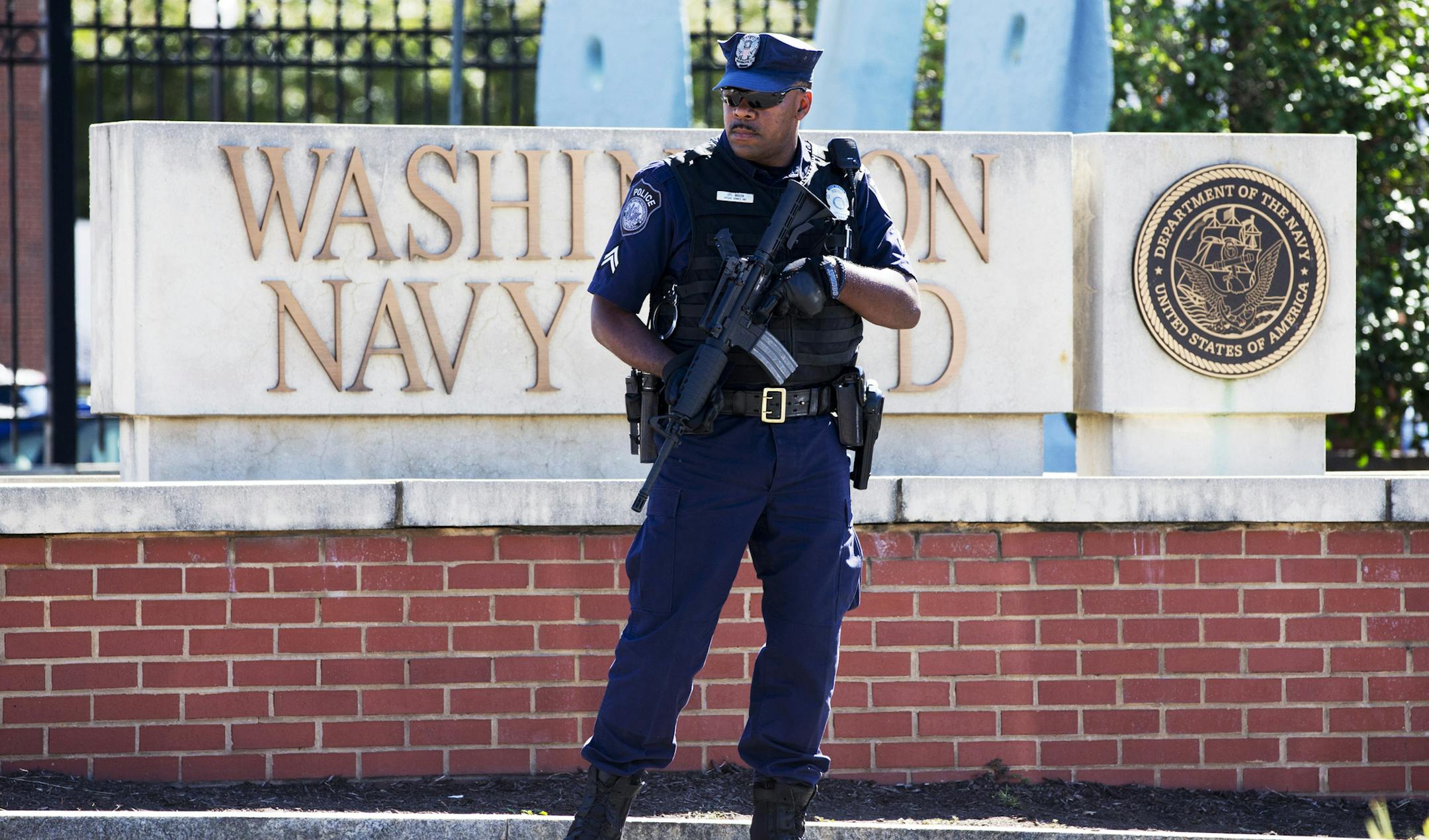 FILE - This Sept. 17, 2013 file photo shows an armed officer who said he is with the Defense Department, standing near guard the gate at the Washington Navy Yard the day after a gunman launched an attack inside the Yard. An independent review triggered by the Washington Navy Yard killings last year says threats to Defense Department personnel and facilities increasingly are coming from within. It says the department must rethink its outdated security theory that suggests defending the perimeters