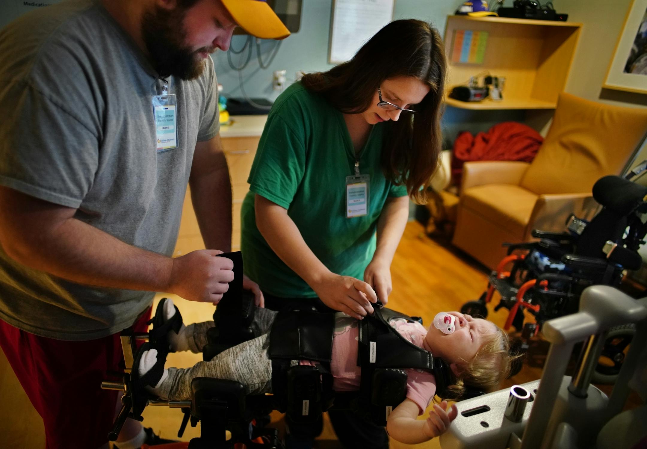 Dylan and Haley Long help get their daughter Aria into a vertical wheelchair, which feels scary for the 17-month old.
