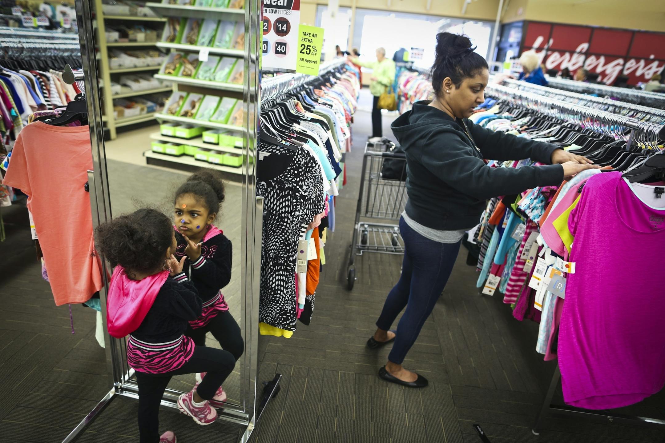 Sharmi Richardson past the time, while her mom Daya Parsons shopped, putting colored stickers on her face from the sticker deals on clothes during opening day of the Herberger's Clearance Center on Thursday, May 15, 2014, in Maplewood, Minn.