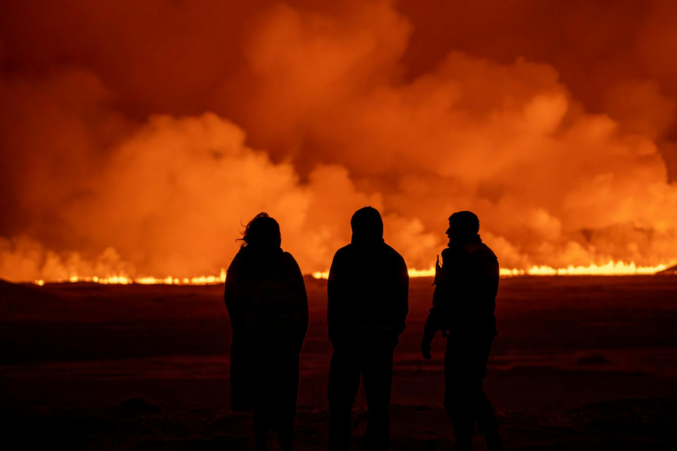 People watch as the night sky is illuminated by the eruption of a volcano in Grindavik on Iceland's Reykjanes Peninsula, Monday, Dec. 18, 2023. (AP Photo/)