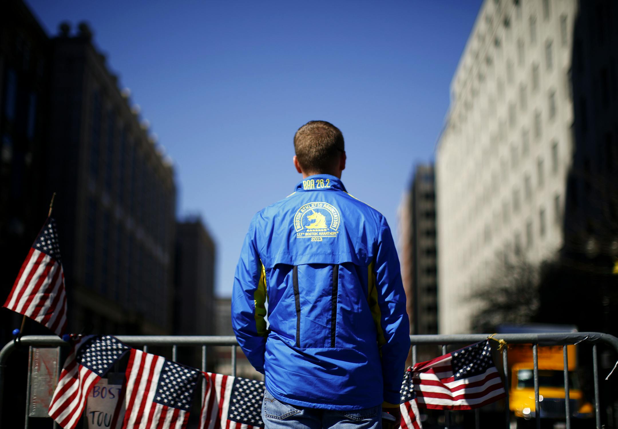 A man with a jacket from the 2013 Boston Marathon visits a makeshift memorial at the corner of Boylston and Berkeley Streets in Boston, April 17, 2013. A lid from one of the pressure cookers that investigators believe were used in the bombings at the Boston Marathon on Monday was found on a rooftop, giving a sense of the force of the blast. (Eric Thayer/The New York Times)