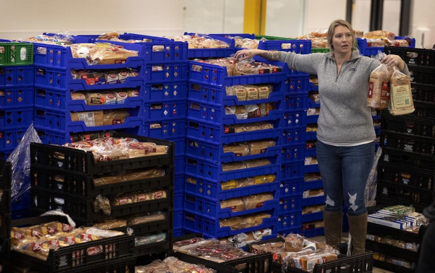 Megan Struxness of Minneapolis a volunteer , gathers loaves of bread at Second Harvest . Staff and volunteers at Second Harvest Heartland, the state's largest food bank, will be busy filling emergency food kits in response to the coronavirus next week at its warehouse in Brooklyn Park. The kits contain an 8-day supply of food, including such items as rice, pasta, fruit and canned chicken. and will be provided to 10,000 impoverished families who may be particularly at risk of the virus .