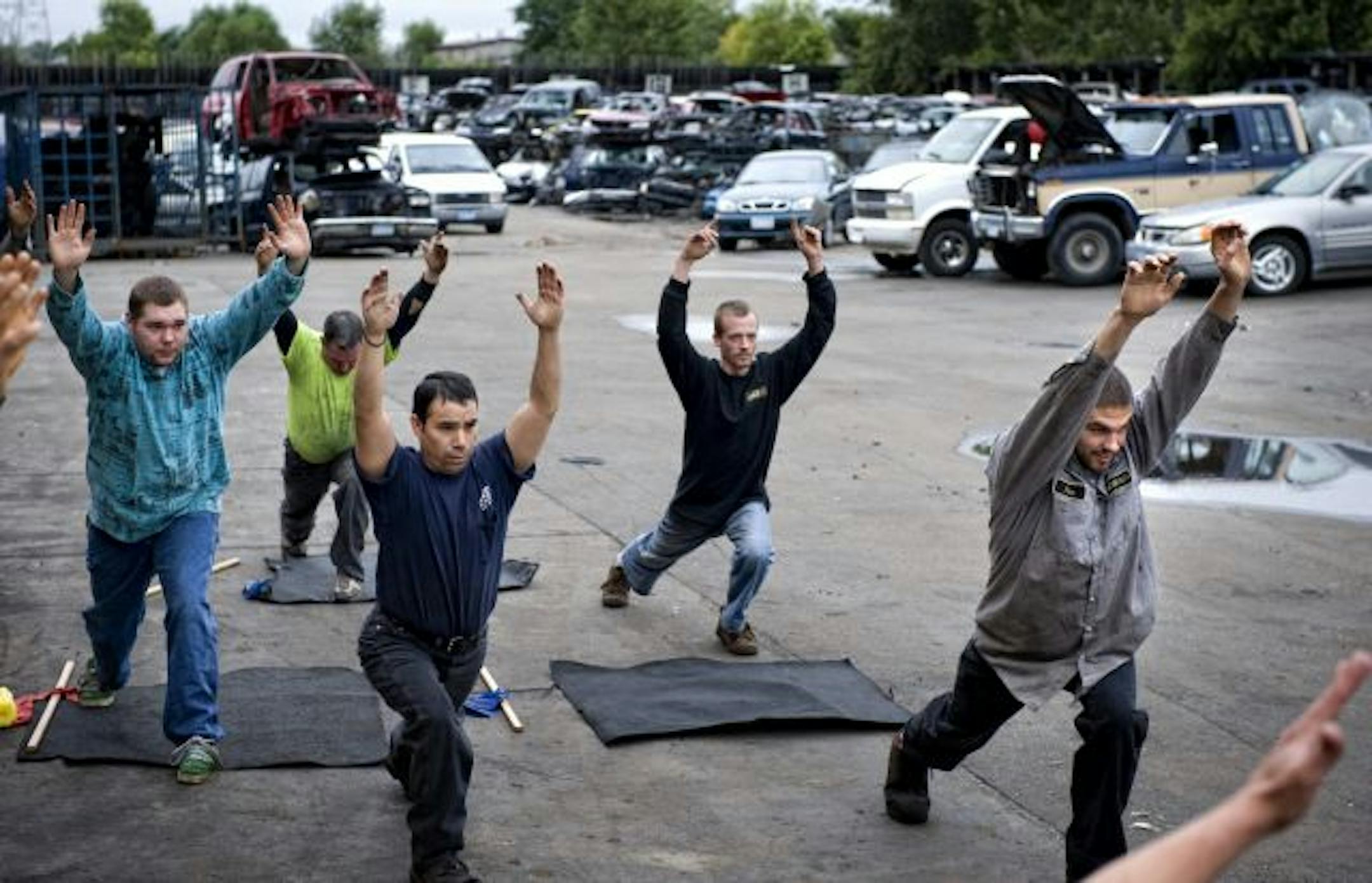 The dismantlers of Ace Auto in St. Paul gather weekly in the junkyard for required Pilates instruction. For a mat, they use old carpet pulled from car trunks.