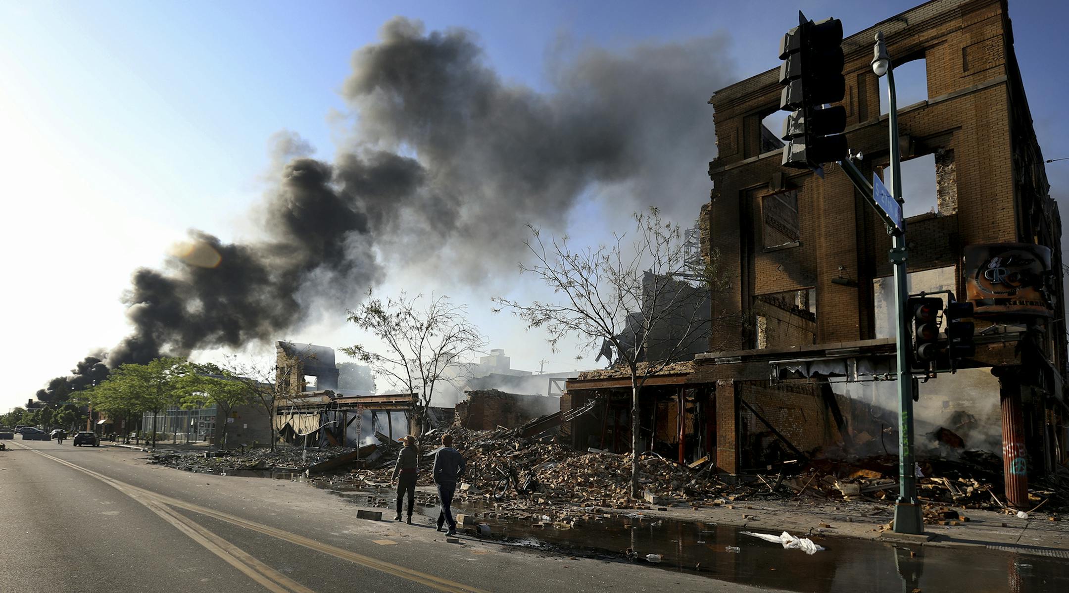 People survey the damage along Lake St. near S. 27th Ave. as a fire burns to the east following protests in the death of George Floyd, Saturday, May 30, 2020, in Minneapolis, Minn. Floyd died after an officer pressed his knee into his neck for several minutes even after he stopped moving and pleading for air. (David Joles/Star Tribune via AP)