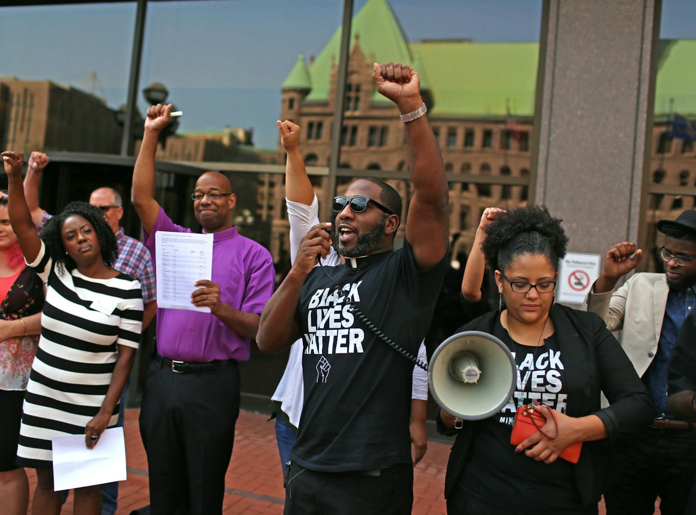 Pastor Danny Givens Jr., of Above Every Name Ministries, speaks at the BLM (Black Lives Matter) rally on the plaza of the Hennepin County Government Building Tuesday at 1p.m. Others (l-r) are Phyllis Hill, lead organizer for ISAIAH (b/w dress), Rev. Dewayne Davis (purple), and Kandace Montgomery, one of those charged (with bullhorn at right). The rally was to support Black Lives Matters defendants who were in court tuesday for a key hearing on a number of motions related to protests at Mall of A