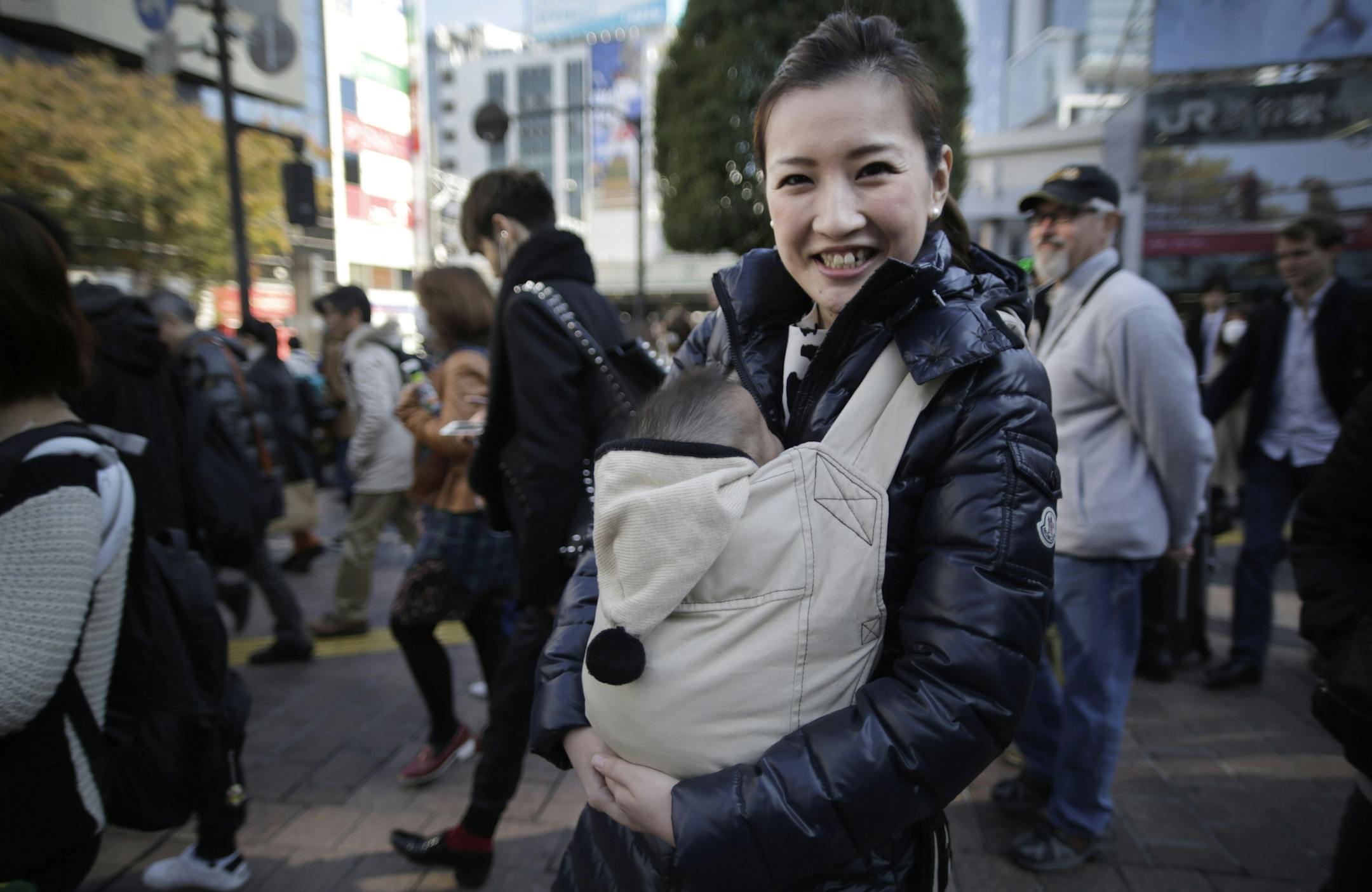 In this Friday, Nov. 21, 2014 photo, Mai Yamaguchi, a 29-year-old trading company employee heading into the gaudy Shibuya shopping area for an outing with her 4-month-old son and two other young moms and babies, poses for a portrait at a scramble crossing in Shibuya in Tokyo. Japanese Prime Minister Shinzo Abe’s choice last week to postpone a sales tax hike to help fend off recession comes less as a relief than as cause for greater concern over how the country will cope with its balloonin