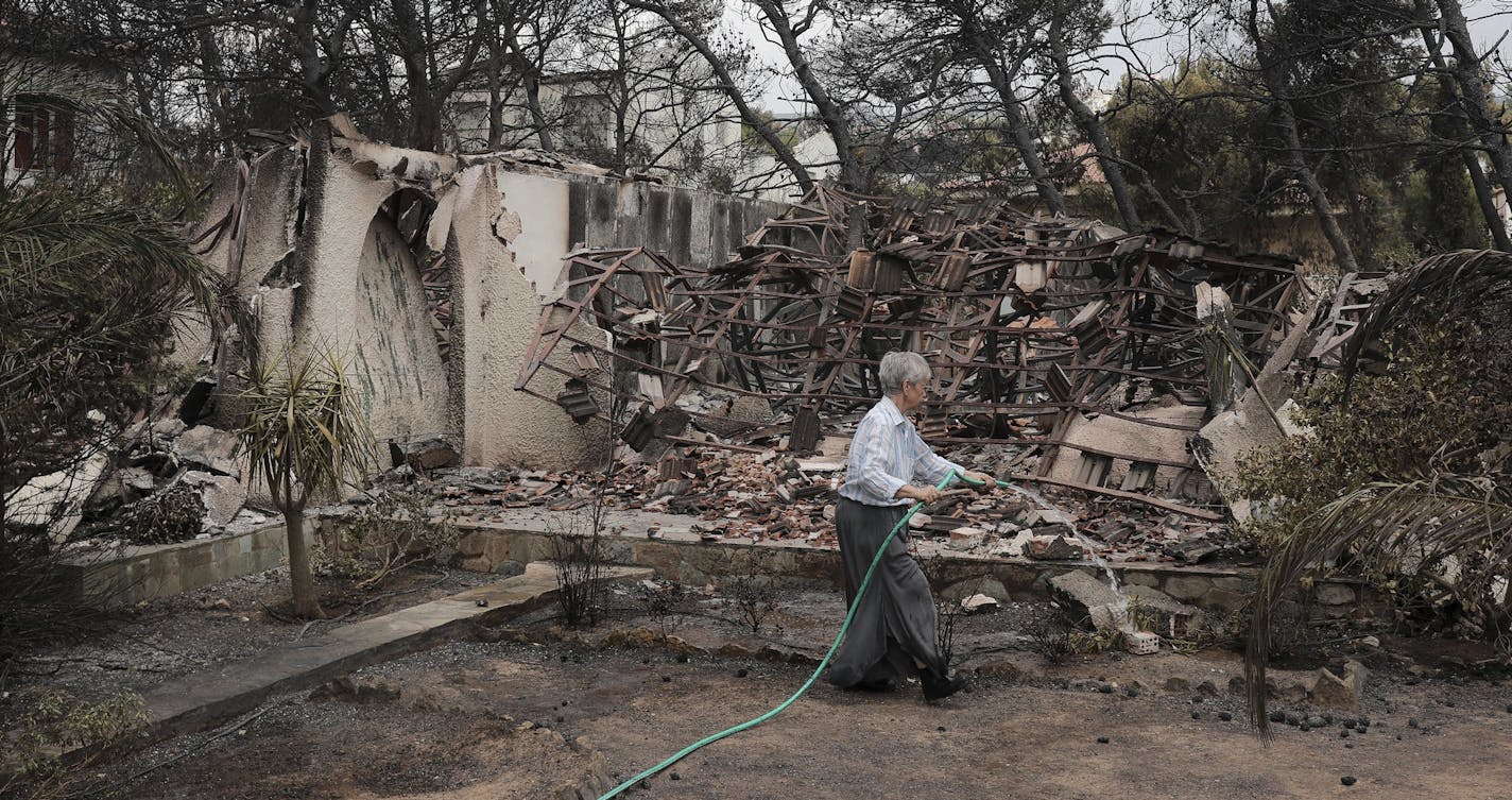 A woman sprays water outside her house that was damaged in the wildfires near the village of Neos Voutzas near Athens, Tuesday, July 24, 2018. Greece sought international help through the European Union as fires on either side of Athens left lines of cars torched, charred farms and forests, and sent hundreds of people racing to beaches to be evacuated by navy vessels, yachts and fishing boats.(AP Photo/Yorgos Karahalis)