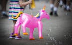 A child, carrying a blow-up unicorn, is captivated by bubbles from a vendor at the fair.