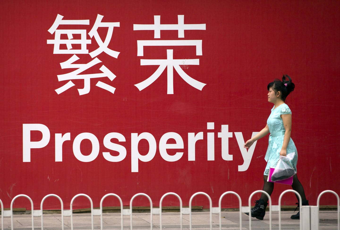 In this July 15, 2015 photo, a woman walks past a sign reading "Prosperity" in Chinese and English in Beijing. China's economic growth decelerated in the latest quarter but relatively robust spending by Chinese consumers helped to avert a deeper downturn. The world's second-largest economy grew by 6.9 percent in the three months ended in September, the slowest since early 2009 in the aftermath of the global crisis, data showed Monday, Oct. 19, 2015. That was down from the previous quarter's 7 pe