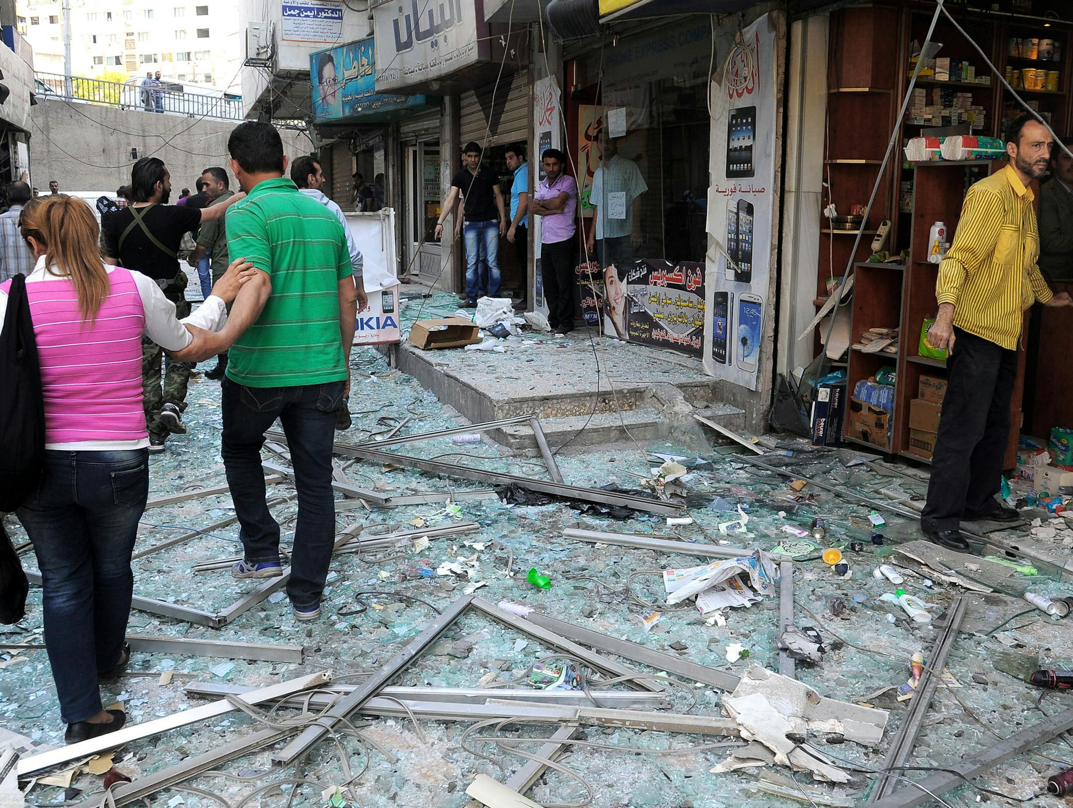 In this photo released by the Syrian official news agency SANA, Syrians walk on shattered glass from damaged shops at the scene of a powerful explosion which occurred in the central district of Marjeh, Damascus, Syria, Tuesday April 30, 2013. A powerful explosion rocked Damascus on Tuesday, causing scores of casualties, a day after the country's prime minister narrowly escaped an assassination attempt in the heart of the heavily protected capital. (AP Photo/SANA)