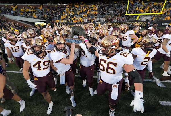 Gophers quarterback Athan Kaliakmanis (8) and defensive lineman Theorin Randle (99) carry the Floyd of Rosedale trophy after their 12-10 win over Iowa