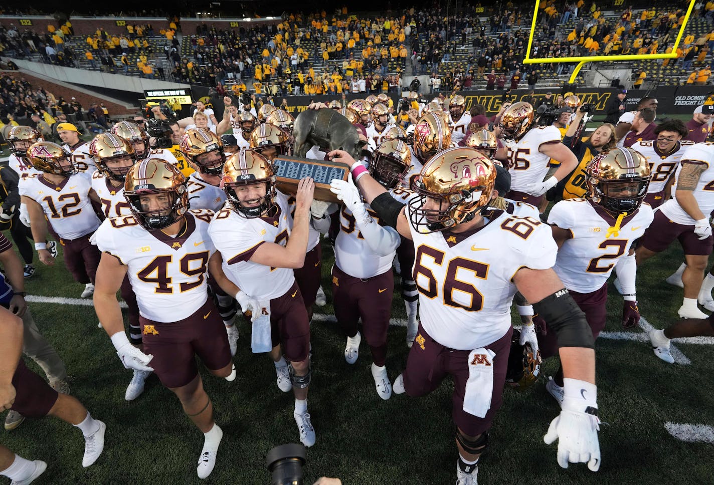 Gophers quarterback Athan Kaliakmanis (8) and defensive lineman Theorin Randle (99) carry the Floyd of Rosedale trophy after their 12-10 win over Iowa on Saturday in Iowa City.