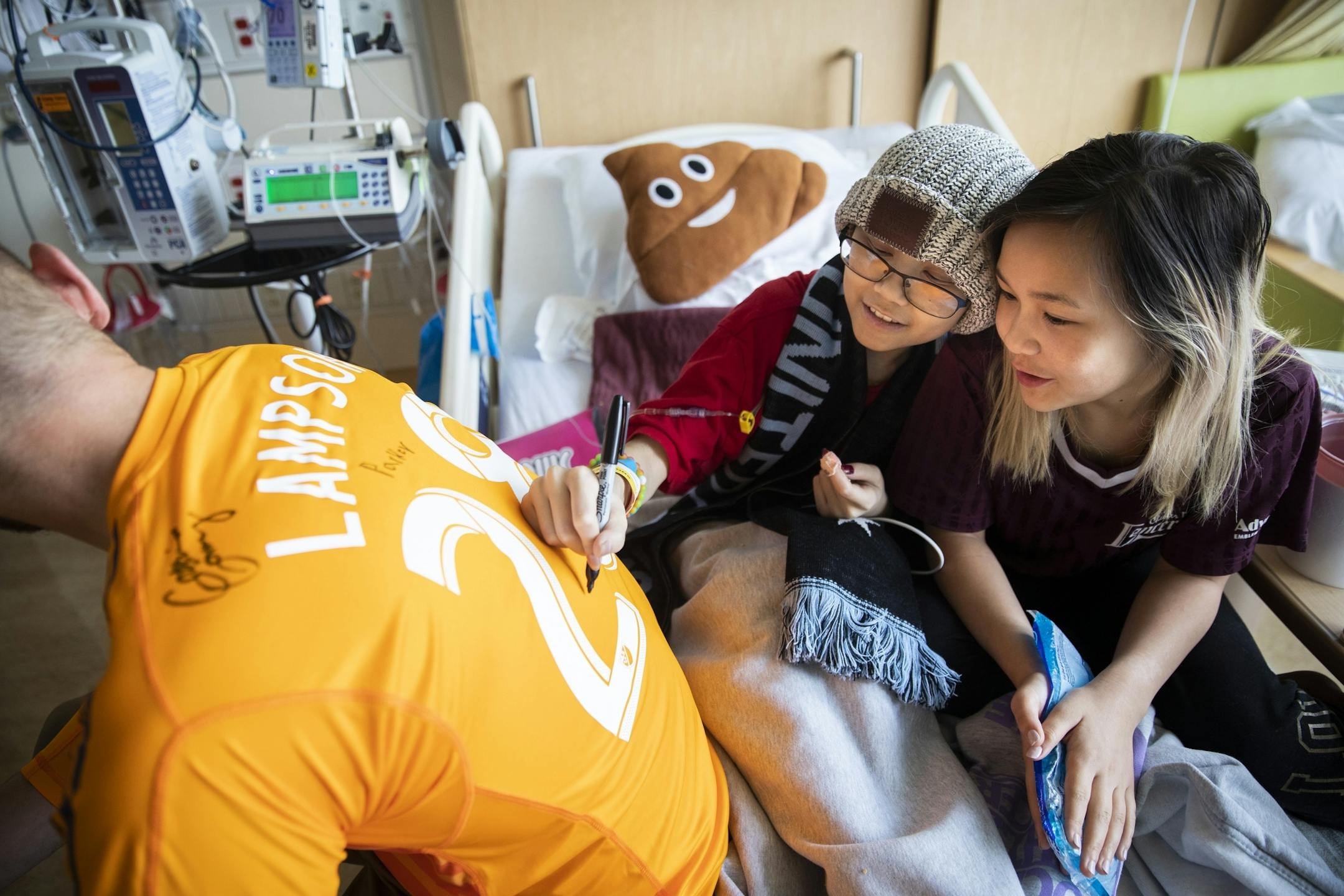 Nathalia Hawley, center, 14, a bone cancer patient, and her sister Gabi Augusta, 10, sign the back of a jersey worn by Minnesota United goalkeeper Matt Lampson during his visit to the hospital.