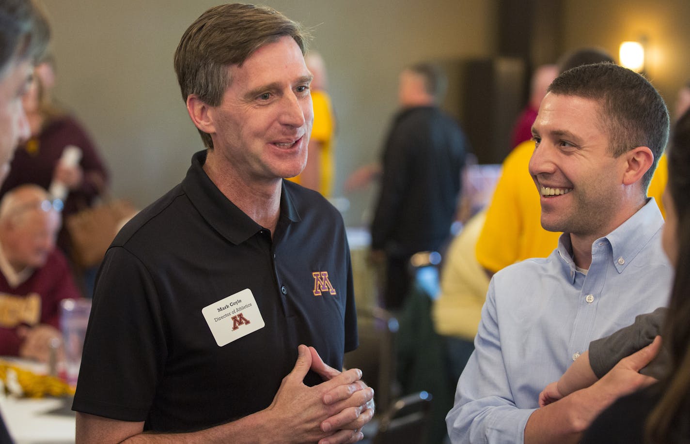 U of M athletic director Mark Coyle, on his second day on his new job, makes his first public appearance at the Crow River Country Club in Hutchinson, Minn. during their first stop of the Gopher Road Trip Chalk Talk. Here, Coyle talks with the Ryan and Emily Ritchie (Son Asher, 7-months-old in Ryan's arms not visible.) Ryan is a Dentist in Hutchinson and is a gopher football and hockey fan. ] Hutchinson, MN - 06/01/2016