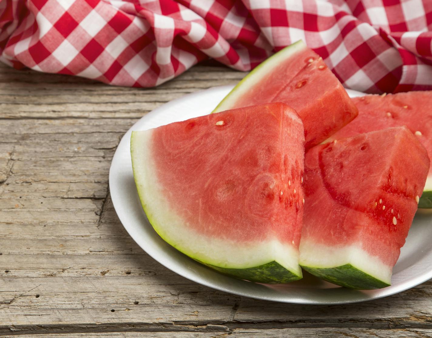 A weathered picnic table with a red and white checkered tablecloth and slices of seedless watermelon. The shot is from a higher angle leaving copy space. The image can be used to illustrate summer, food, summer food, fruit, farmers markets, summer food recipes, picnic, healthy summer food ideas, fourth of July, Labor Day, etc.