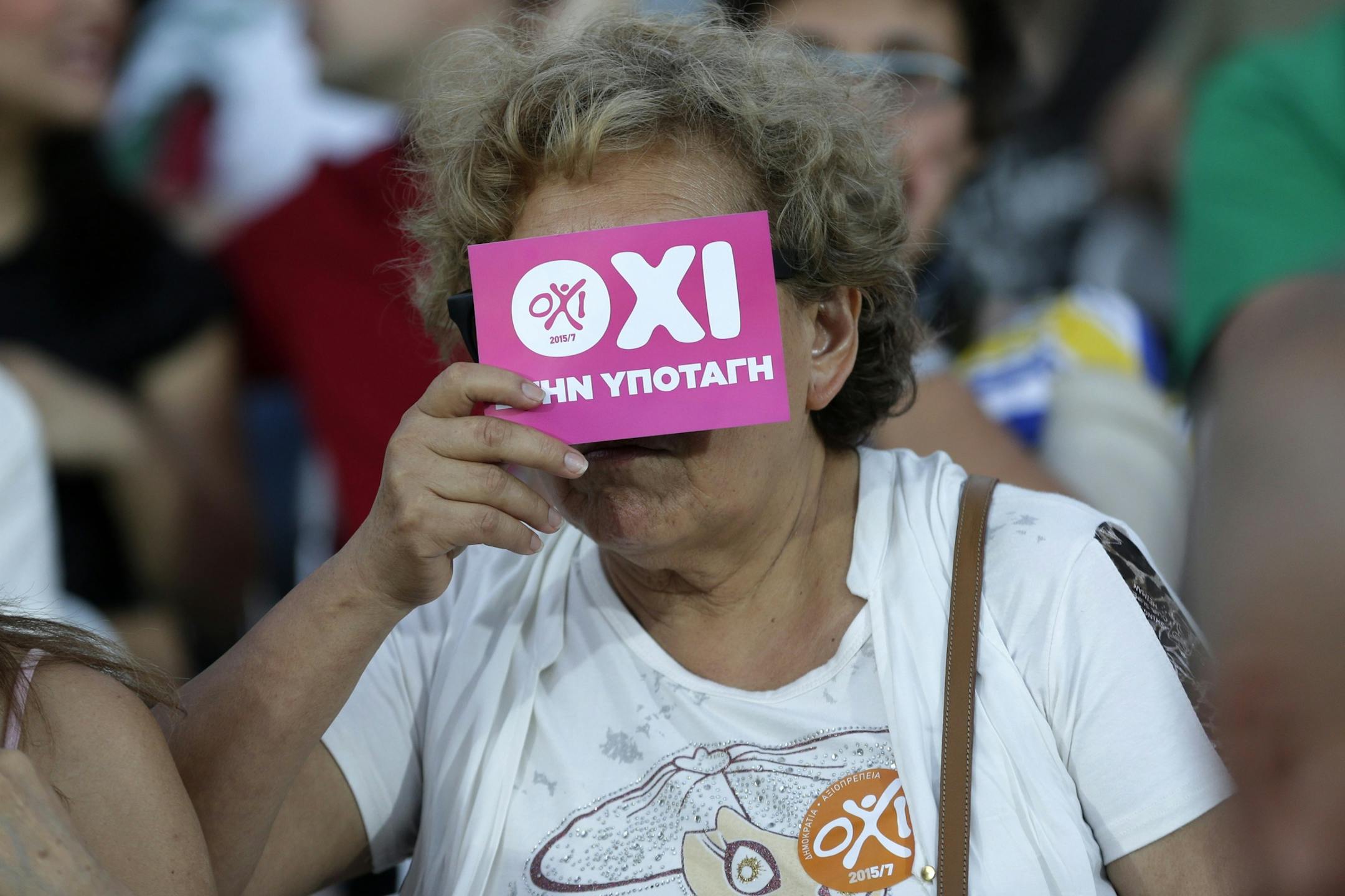 A supporter of the No vote covers her face with a flyer reading ''No to submission'' at Klafthmonos square in Athens, Sunday, July 5, 2015. Greece faced an uncharted future as its interior ministry predicted Sunday that more than 60 percent of voters in a hastily called referendum had rejected creditors' demands for more austerity in exchange for rescue loans.