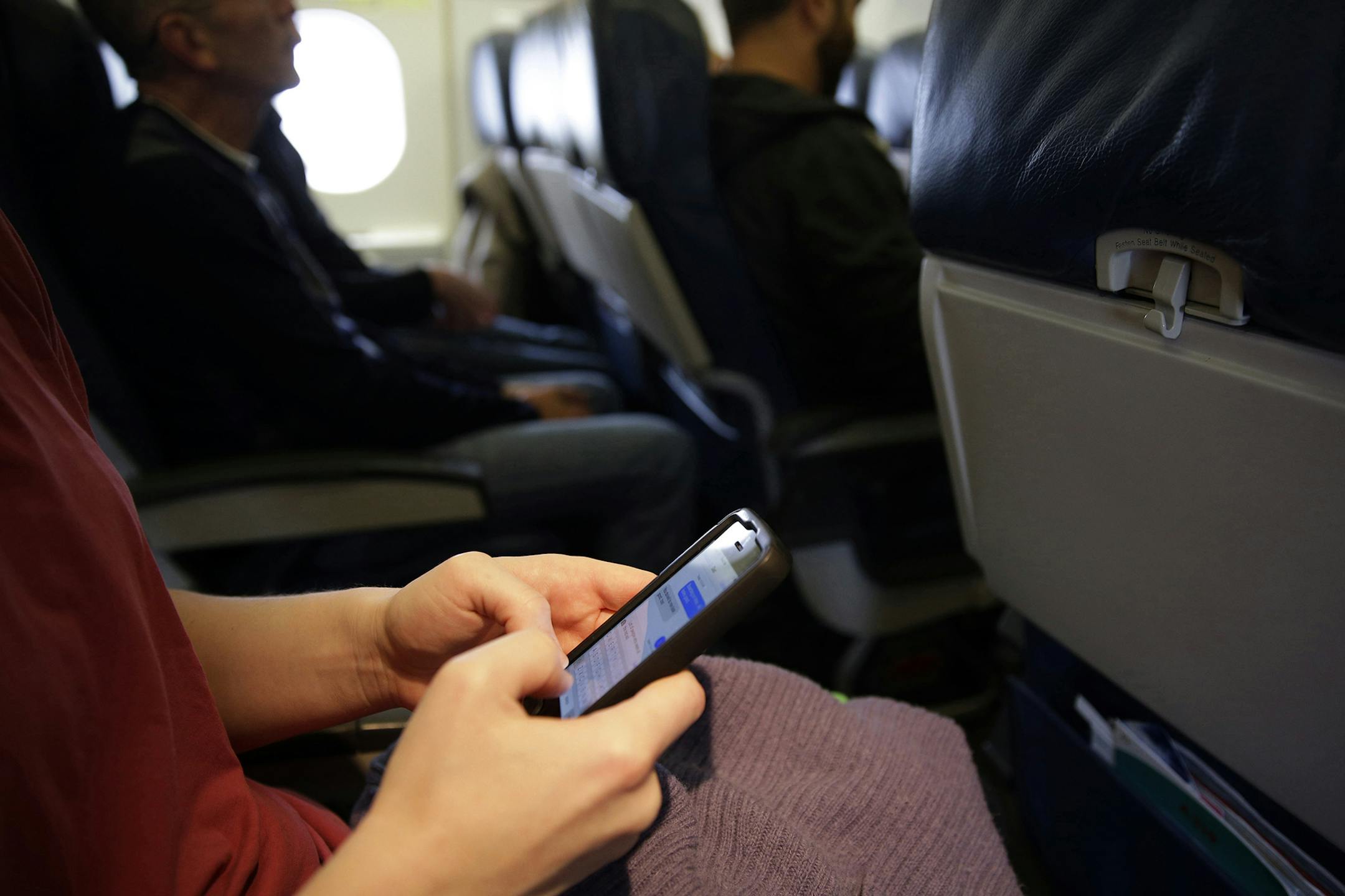 FILE - In this Oct. 31, 2013, file photo, a passenger checks her cell phone before a flight in Boston. The Federal Communications Commission might be ready to permit cellphone calls in flight. Old concerns about electronics being a danger to airplane navigation have been debunked. And carriers could make some extra cash charging passengers to call a loved one from 35,000 feet. But that extra money might not be worth the backlash from fliers who view overly-chatty neighbors as another inconvenien