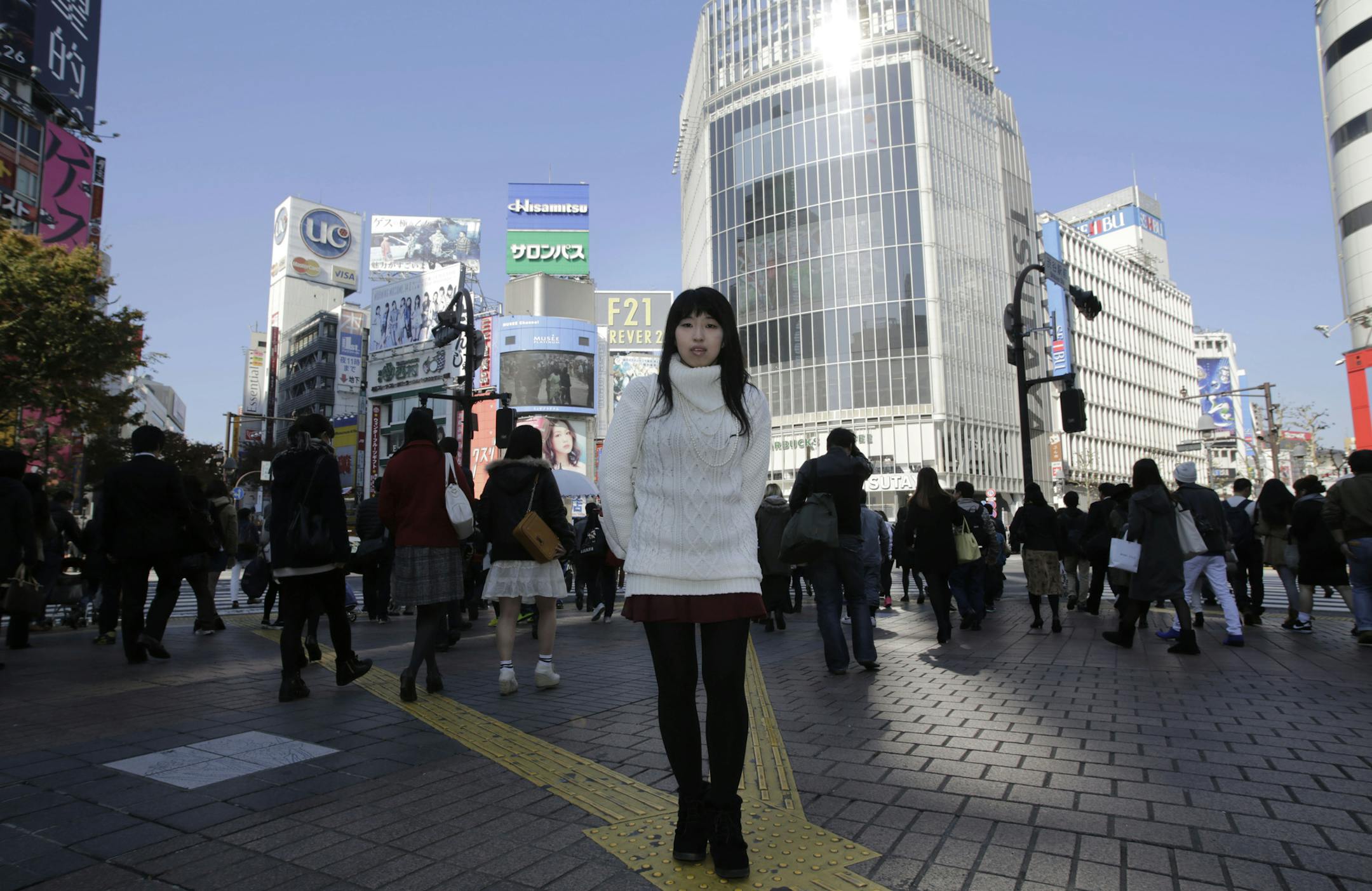 In this Friday Nov. 21, 2014 photo, Kaori Endo, a 21-year-old bread factory worker from Ibaraki, north of Tokyo, poses for a portrait at a scramble crossing at Shibuya shopping district in Tokyo. Japanese Prime Minister Shinzo Abe’s choice tlast week to postpone a sales tax hike to help fend off recession comes less as a relief than as cause for greater concern over how the country will cope with its ballooning national debt. Endo said she wouldn’t mind paying more for taxes if she