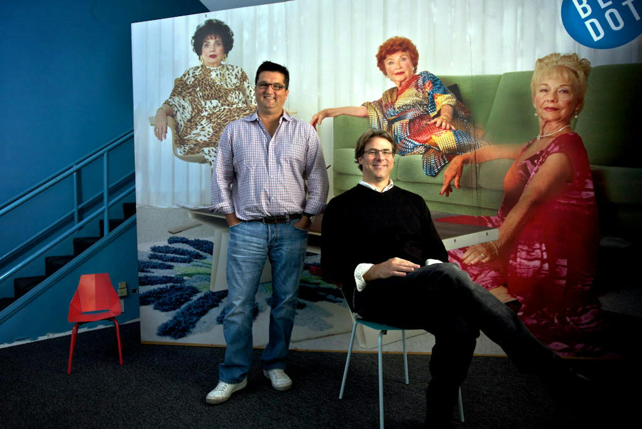 John Christakos, left, and Maurice Blanks pose at the main entrance of their headquarters with a large blowup of one of the pictures in their catalogs.
