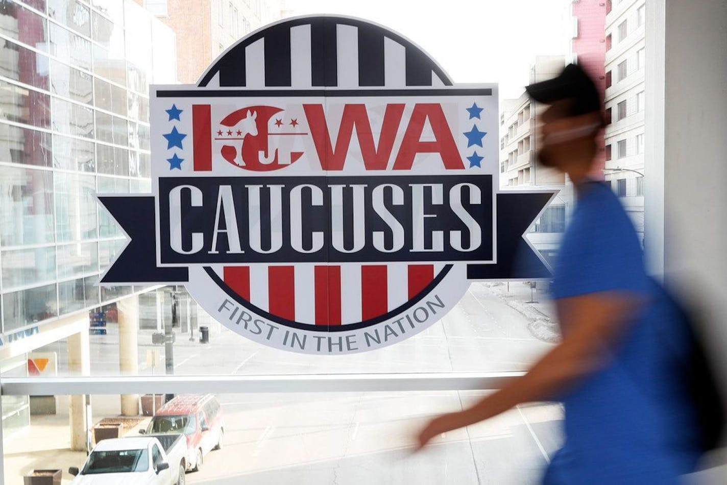 A pedestrian walks past a sign for the Iowa Caucuses on a downtown skywalk, Tuesday, Feb. 4, 2020, in Des Moines, Iowa.