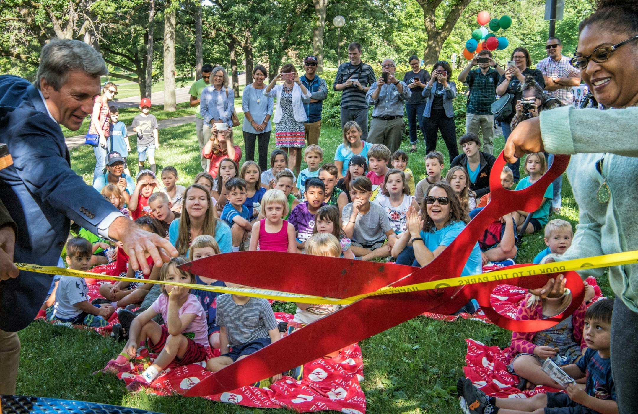 Minneapolis Foundation president and CEO R.T. Rybak and Tyrize Cox of the Minneapolis Parks and Recreation board cut a ceremonial ribbon to open the Little Free Library to the kids.