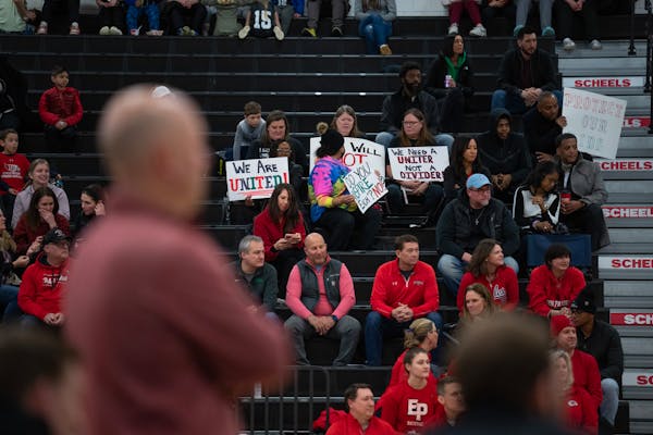Eden Prairie Eagles head coach David Flom coached from the sideline, foreground, while half a dozen people in the stands held up signs during the Eden