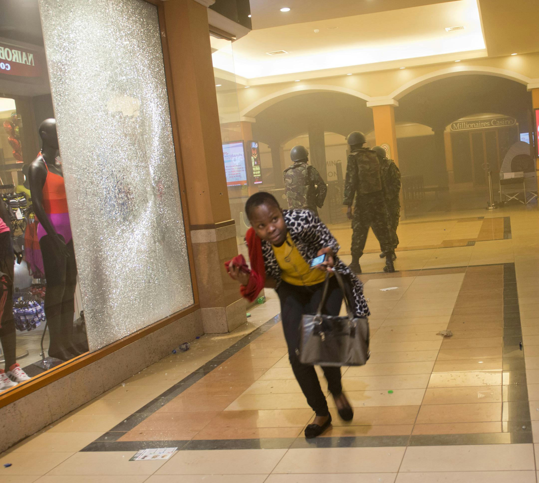 FILE - In this Saturday, Sept. 21, 2013, file photo, a woman who had been hiding during the gun battle runs for cover after armed police enter the Westgate Mall in Nairobi, Kenya, after gunmen threw grenades and opened fire Saturday, killing at least 22 people in an attack targeting non-Muslims at the upscale mall. First-hand accounts of the chaotic first hours of the four-day siege of Kenya's posh Westgate Mall are beginning to emerge. (AP Photo/Jonathan Kalan, File)