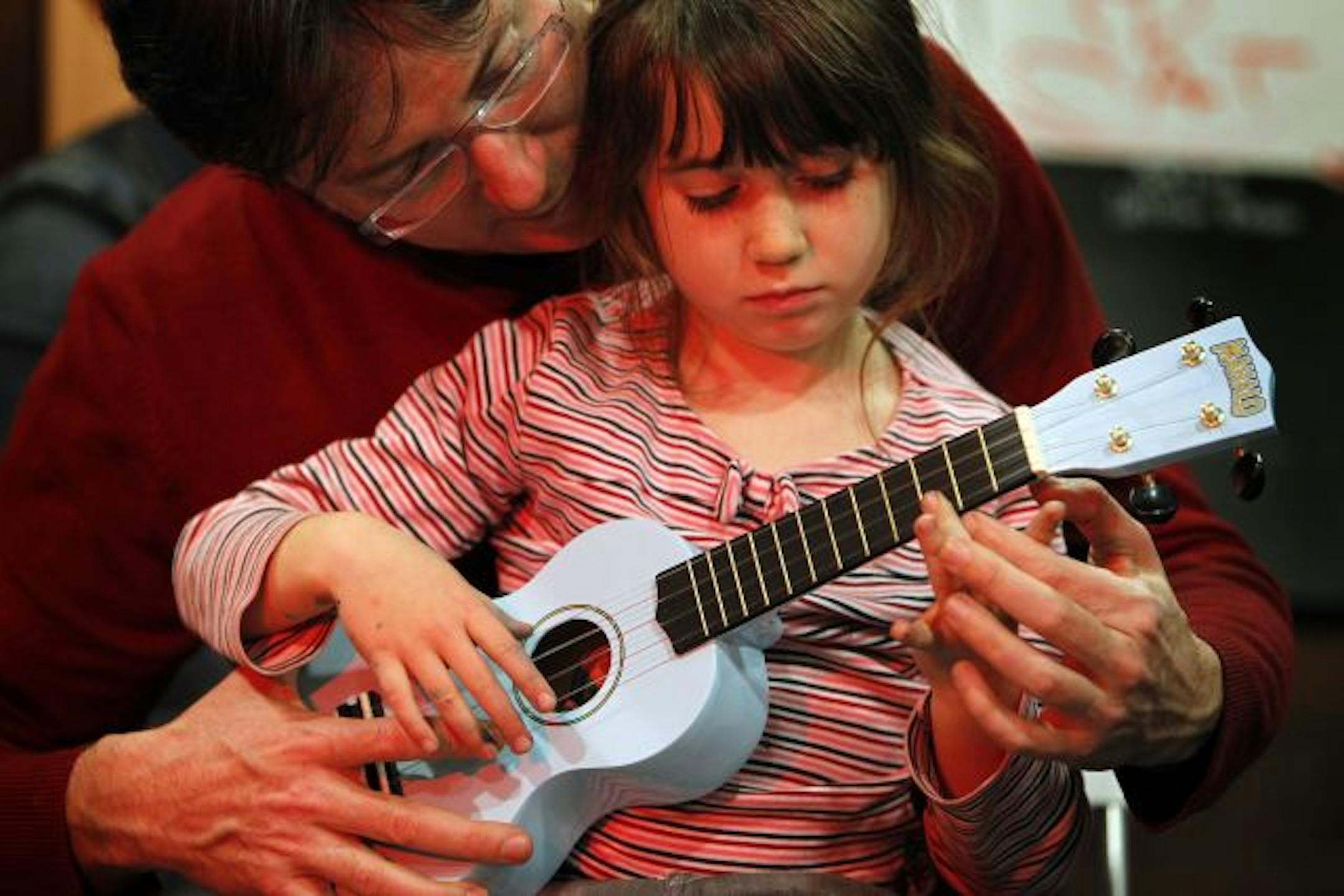 Grace Neis, 5, gets some help playing a ukulele from her father, Greg, during a class at Twin Town Guitars in Minneapolis.