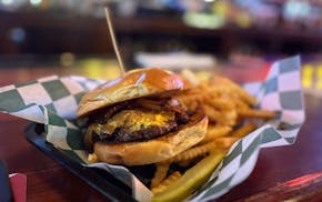 In a basket on an old bar is a burger with cheese, carmelized onions on a bun with a toothpick through it and fries on the side.