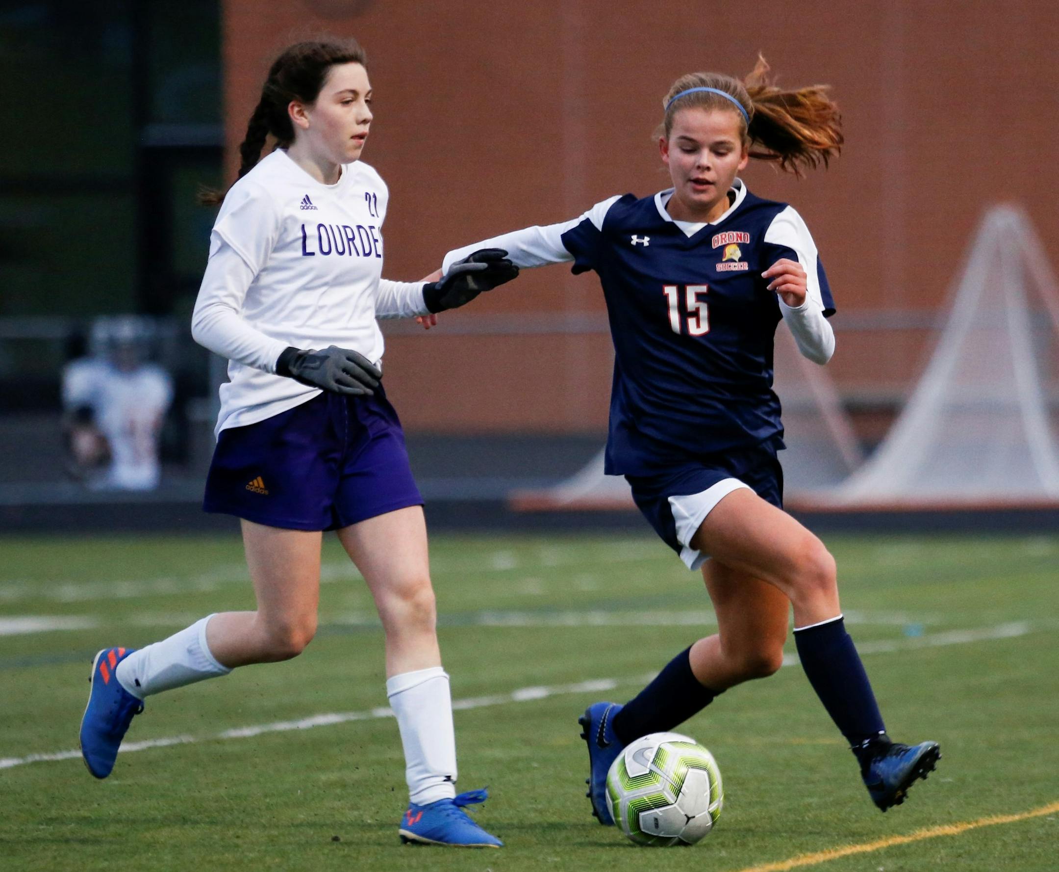 Orono’s Nora Chouanard (15) races after a loose ball as Lourdes’ Grace Buntrock (21) pursues. Chouanard scored late in the first half to give the Spartans a 1-0 lead over the Eagles. Photo by Jeff Lawler, SportsEngine