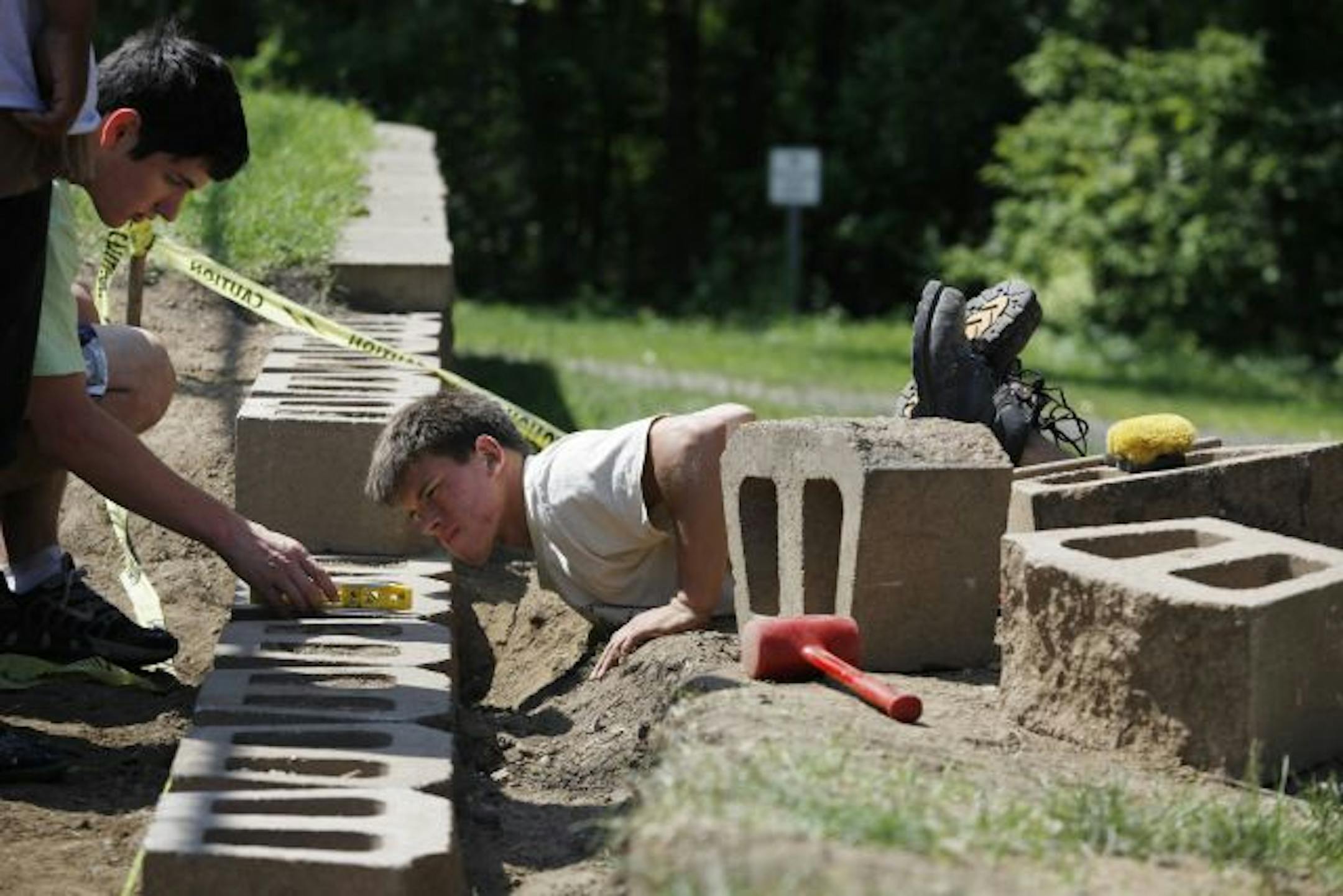 Joey Welle 17 left helped co-worker Dimitri Johnson 18 level off concrete blocks used on a retaining wall at Groveland Park in Inver Grove Heights. The teenagers were hired by Tree Trust, a non-profit that has been hiring kids into summer jobs for years.