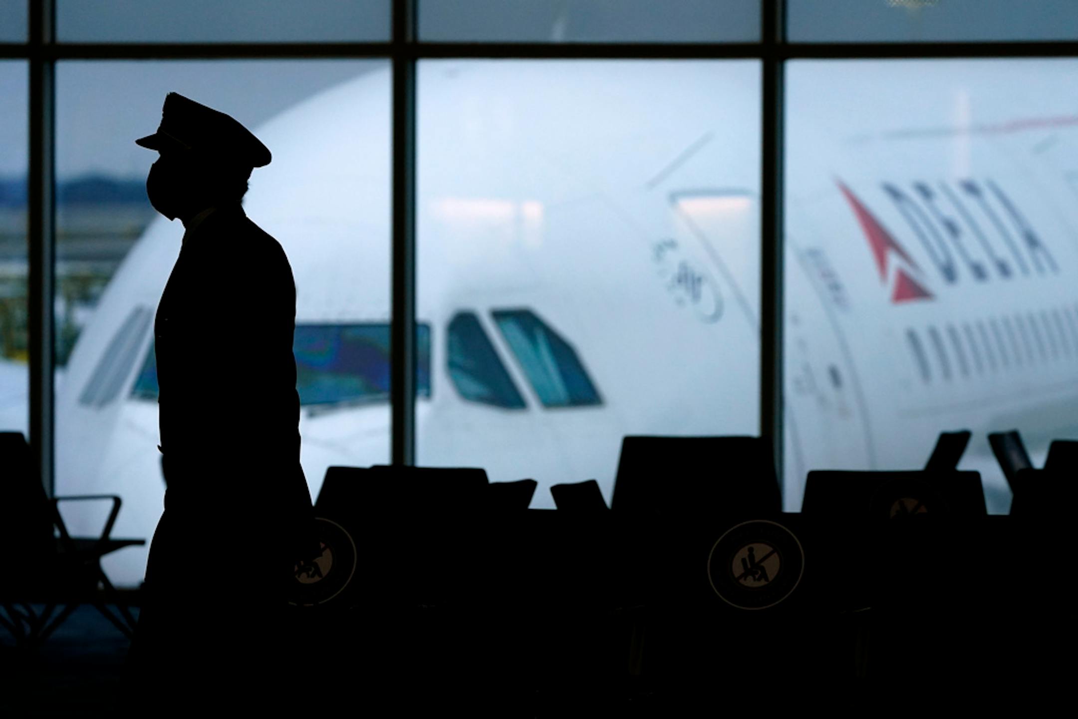 FILE - A Delta Airlines pilot wears a face mask as he walks through a terminal at Hartsfield-Jackson International Airport in Atlanta, on Thursday, Feb. 18, 2021. Airlines executives told legislators on Wednesday, Dec. 15 they are having trouble hiring pilots, flight attendants and other personnel, and that's part of what is causing canceled flights and scrapping of service to some airports. (AP Photo/Charlie Riedel, File)