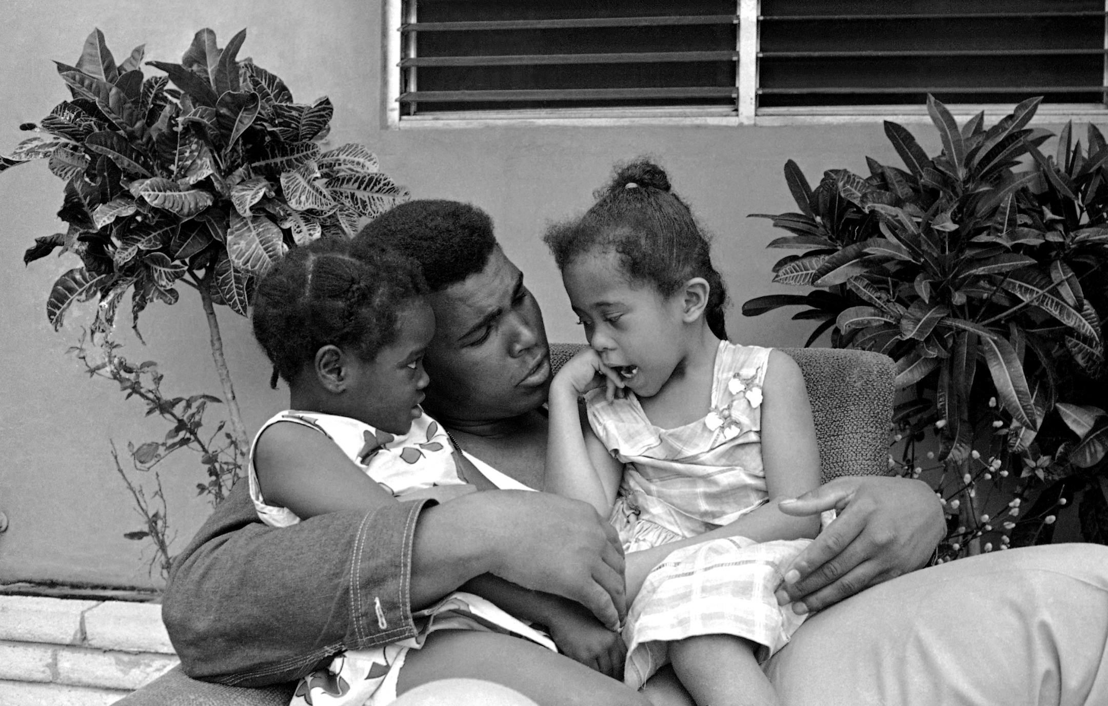 World heavyweight boxing champion Muhammad Ali ?Cassius Clay? is the idol of his neighborhood on March 20, 1965 in Miami, Fla. Two girls from across the street, Margaret Ann Wilson, left and Yolanda Parks are entertained by the champ. (AP Photo) ORG XMIT: APHS283161