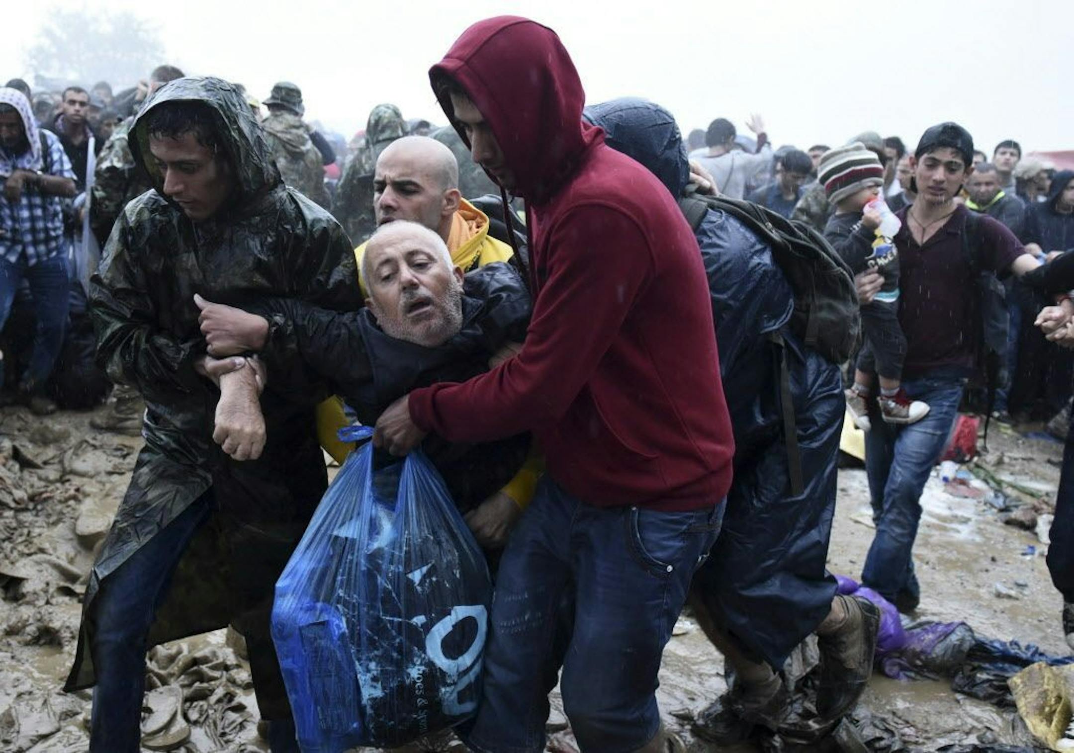 Migrants help an elderly man to pass from the northern Greek village of Idomeni to southern Macedonia, Thursday, Sept. 10, 2015. Thousands of people, including many families with young children, braved torrential downpours to cross Greece�s northern border with Macedonia early Thursday, after Greek authorities managed to register about 17,000 people on the island of Lesbos in the space of a few days, allowing them to continue their journey north into Europe.