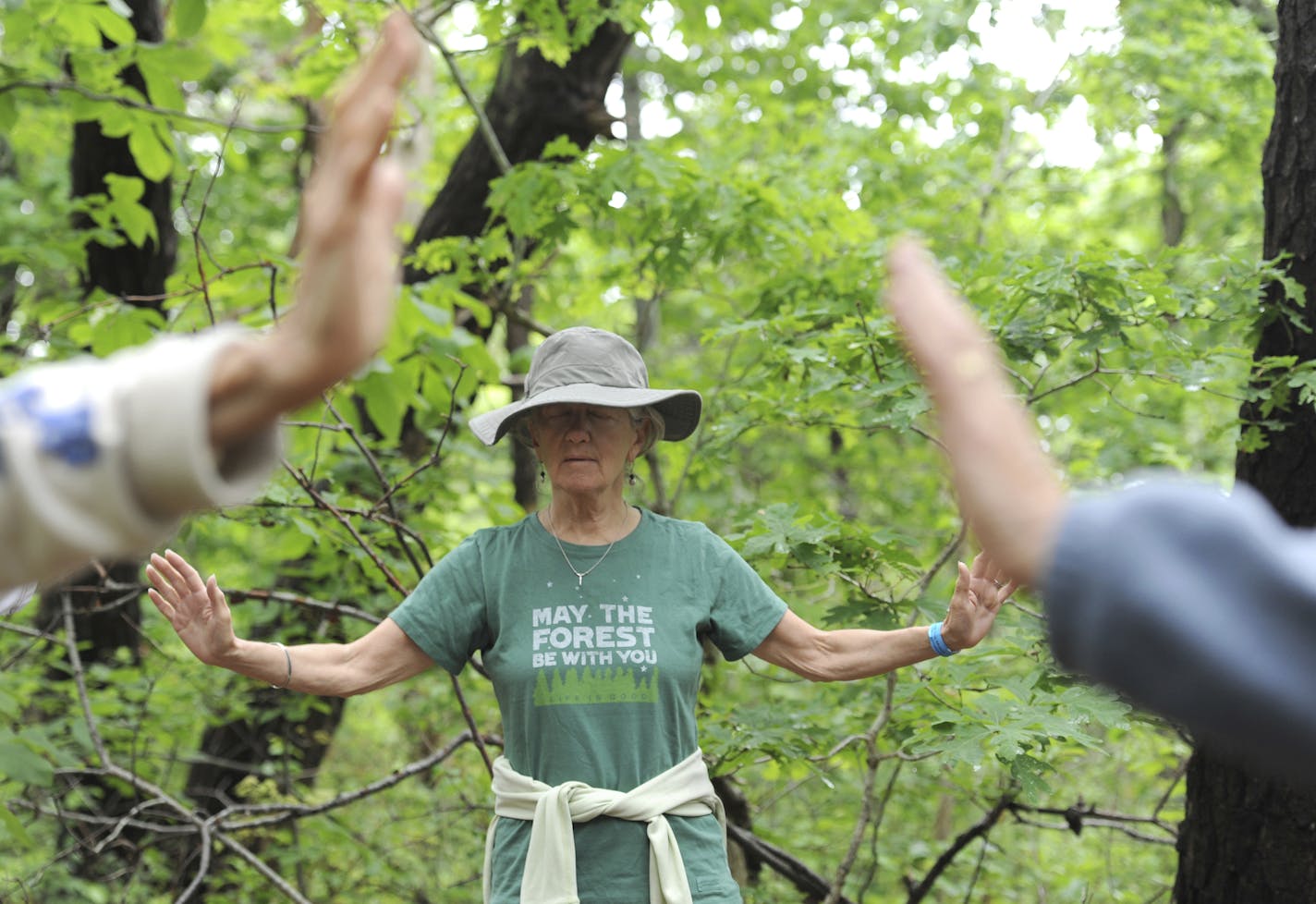 In this June 19, 2019 photo, Janice Joyce, of Albany, N.Y., closes her eyes and spreads her arms out in an energy connection exercise lead by Carol Marcy in Brewster, Mass. Marcy leads a series of meditative nature walks called "forest baths" that is a part of a Japanese practice called Shinrin-yoku. She lead a small group through the trails behind the Cape Cod Museum of Natural History. (Merrily Cassidy/The Cape Cod Times via AP) ORG XMIT: MER566d0fbaa4f90a9d0d16abb4063f9