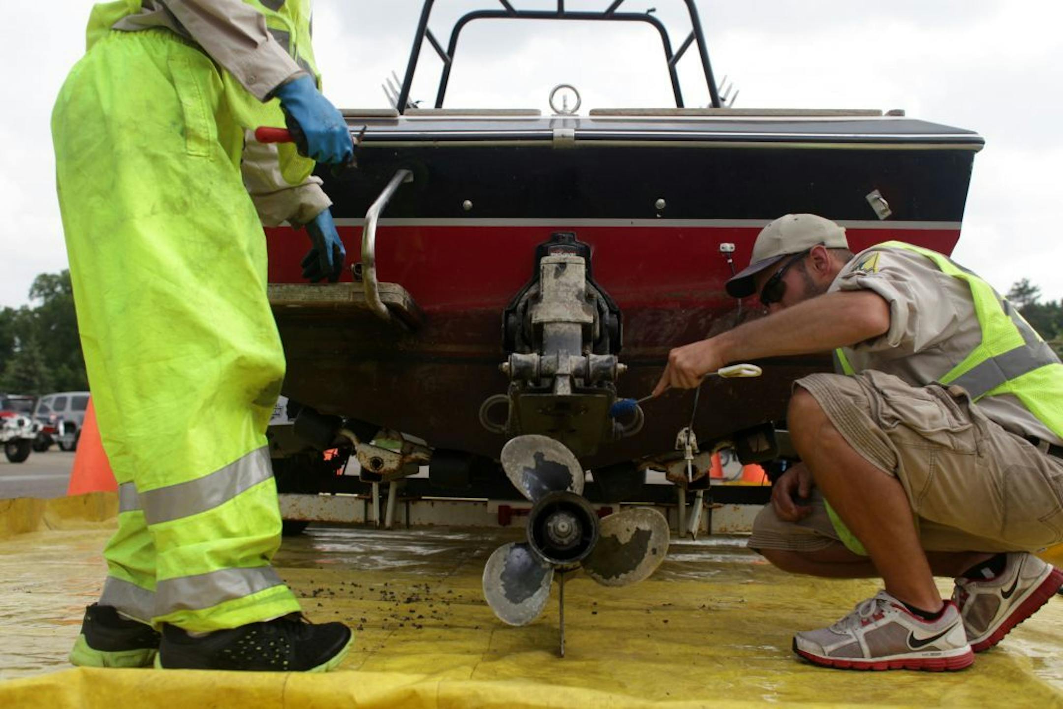 Joe Hale and Ben Troop, DNR Watercraft Inspectors, scrub dead zebra mussels off a boat that had been fined $300 for not following aquatic invasive species laws, at Gray's Bay boat ramp on Thursday afternoon.