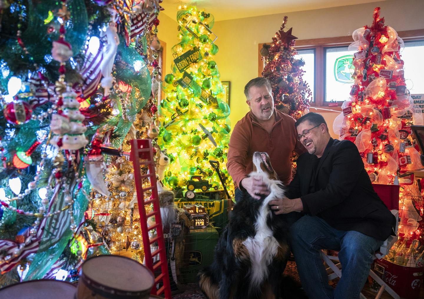 Christmas enthusiast Kevin Milton, right, with his husband, Bill Emery, and their dog, Maximus, in their holiday tree-filled living room. The themed trees and other festive decor fill every room of their house and set the stage for their annual holiday party.