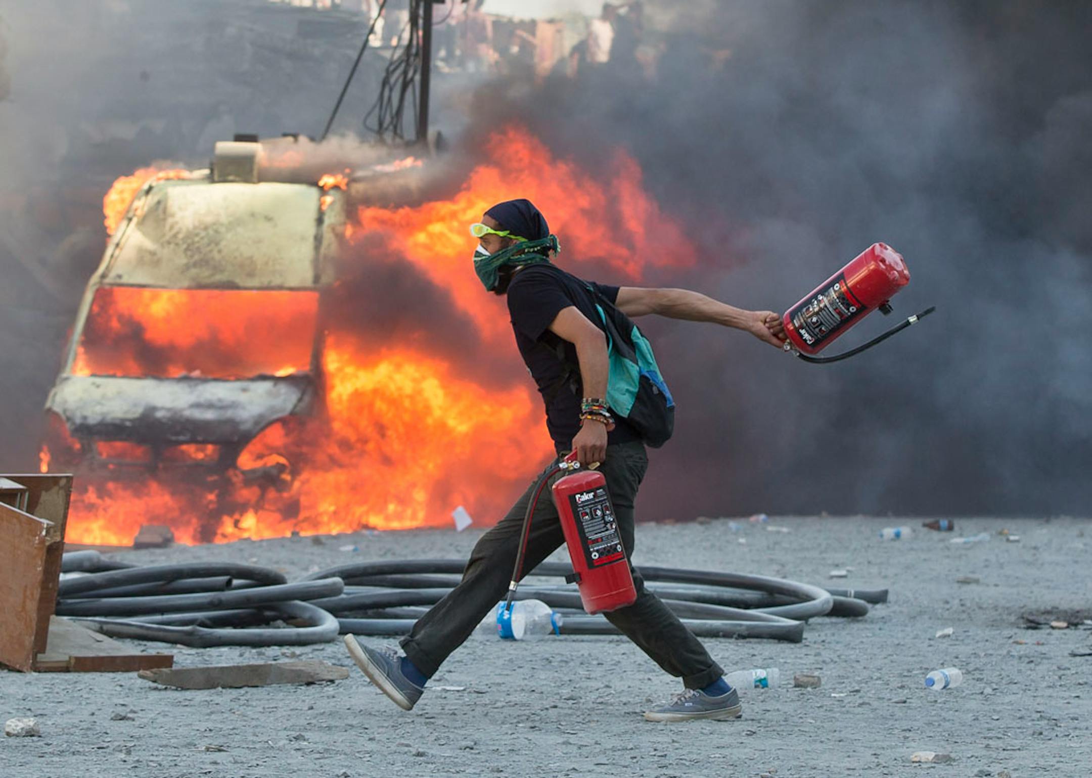A man runs carrying fire extinguishers past a burning van during clashes at the Taksim Square in Istanbul Tuesday, June 11, 2013.