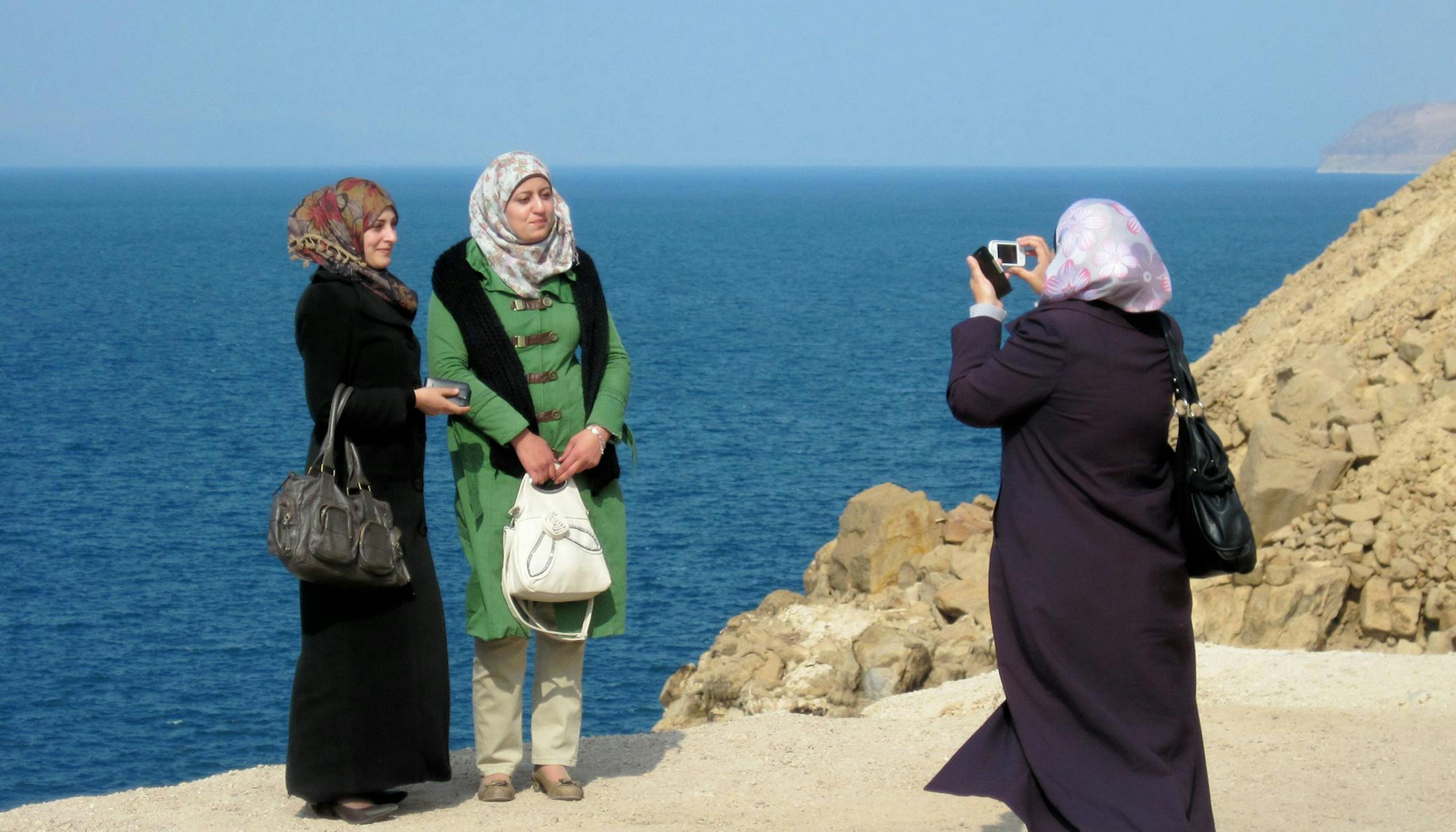 Caption info: Three tourists capture the moment at an overlook along the Jordanian coastline of the Dead Sea. At 400 meters below sea level, the Dead Sea is the lowest point on Earth and its waters contain an extremely high percentage of minerals and salts.