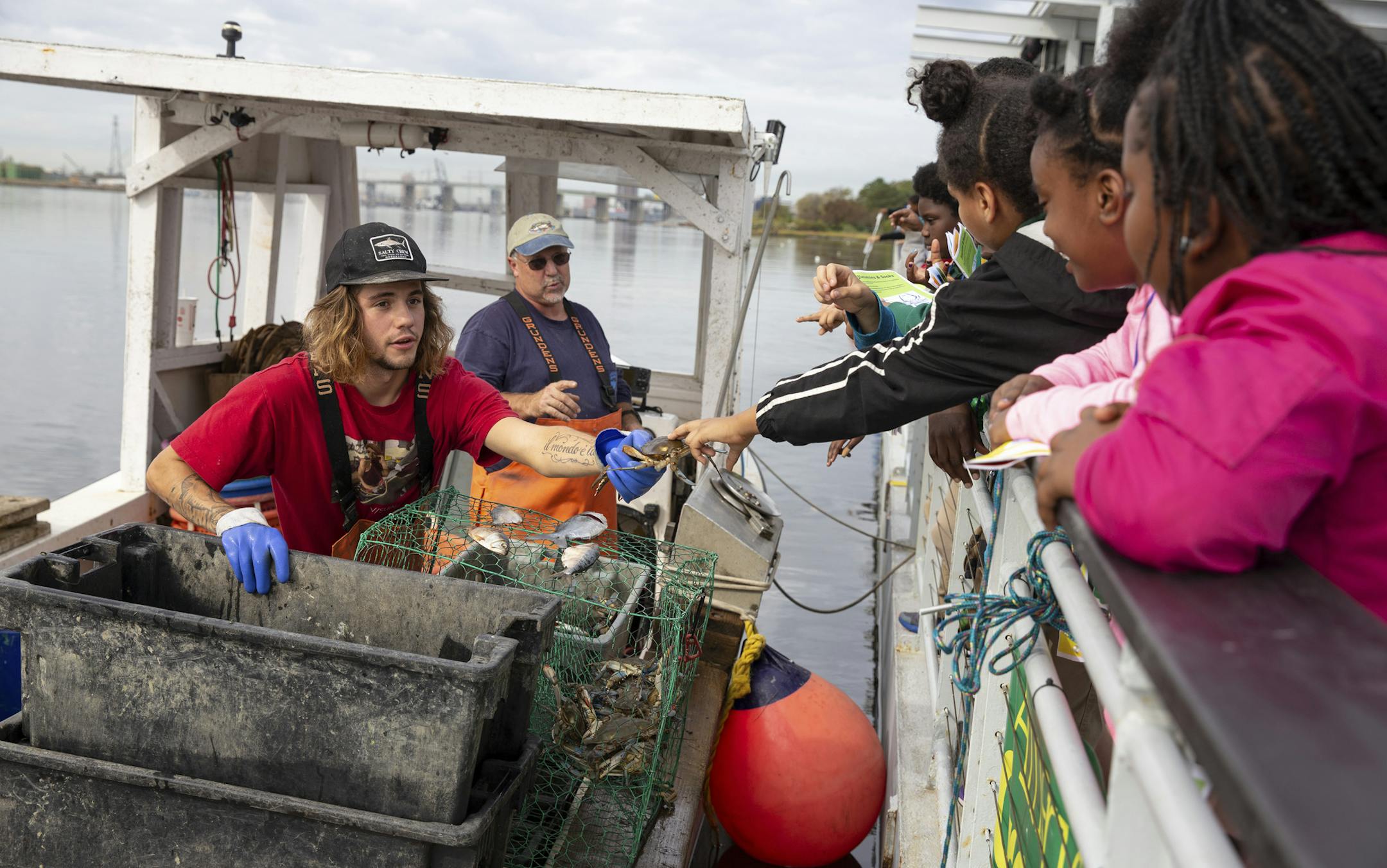 Fourth graders reach out to touch a freshly caught crab during their visit on the Learning Barge in Norfolk, Va., Oct. 25, 2019. Federally funded programs use games, gardens and rain barrels to empower adults and children facing threats like sea-level rise, drought, flooding, extreme heat and severe storms. (Parker Michels-Boyce/The New York Times)