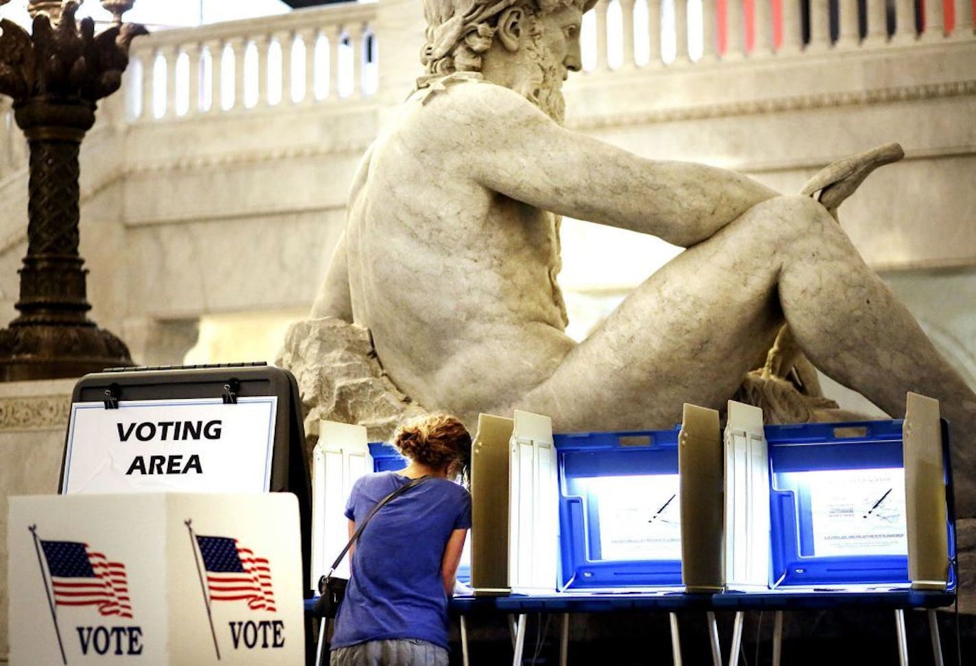 With the Father of Waters sculpture looming to her rear, Kym Spotts of Minneapolis completes her absentee ballot at the Minneapolis City Hall Friday, Aug. 8, 2014, in Minneapolis, MN. Spotts, who said she will be out of town on Tuesday, said she requested the absentee ballot form but received the wrong form in the mail and it turned into a "wild goose chase."