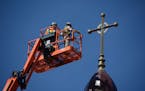 Two men used a telescopic boom lift to reach the top of the former Church of St. Mary in Melrose, Minn., on Monday morning to remove several metal cro