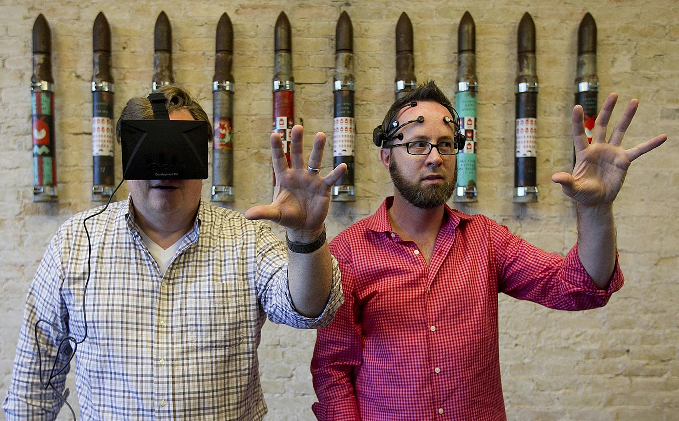 CK Sample, left, wears an Oculus Rift - Virtual Reality Headset for 3D Gaming and reaches for an object envisioned by William "Whurley" Hurley, who is wearing an Emotive EEG Brain Computer Interface. A system developed at Chaotic Moon allows Whurley to envision an object into Sample's 3 dimensional space and to move objects he's thinking about in that space. The company designs wearable technology. (Alberto Martinez/Austin American-Statesman/MCT) ORG XMIT: 1144391