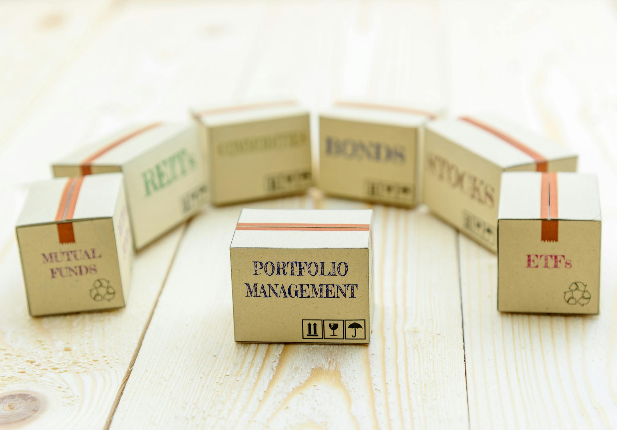 Portfolio and wealth management with risk diversification concept : Small paper cartons / boxes of financial instruments i.e ETFs, REITs, stocks, bonds, mutual funds and commodities, on a wood table.