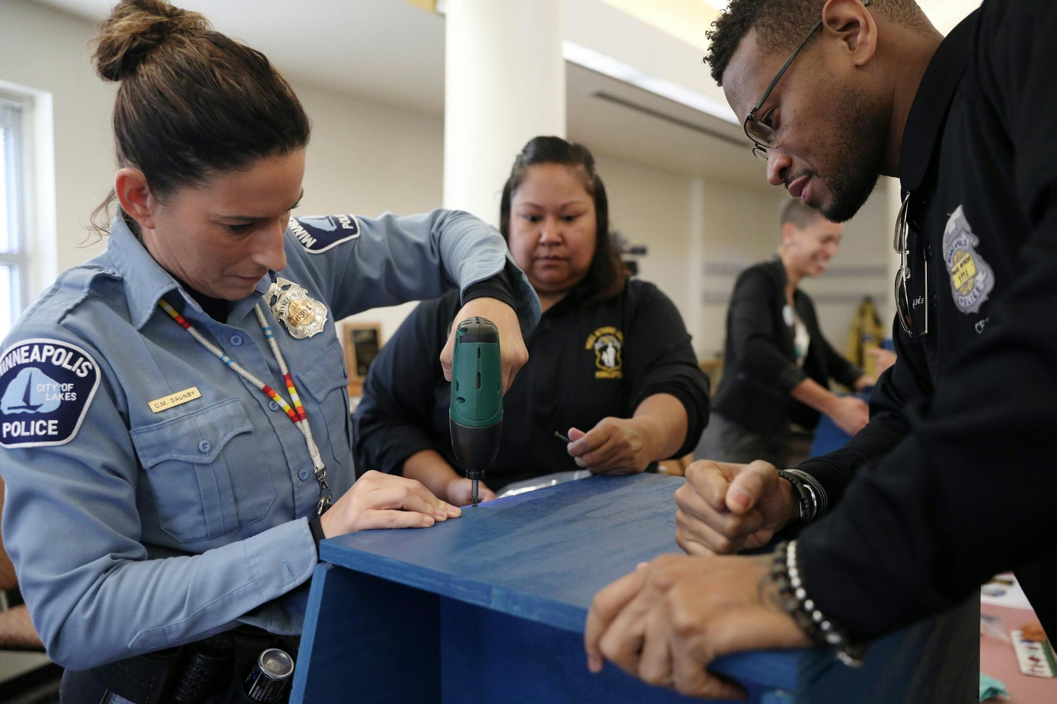 Police officers Colleen Saunby, left, Cheryl Goodman, center, and Jon Edwards, right, worked to build free-standing Little Free Libraries Tuesday.