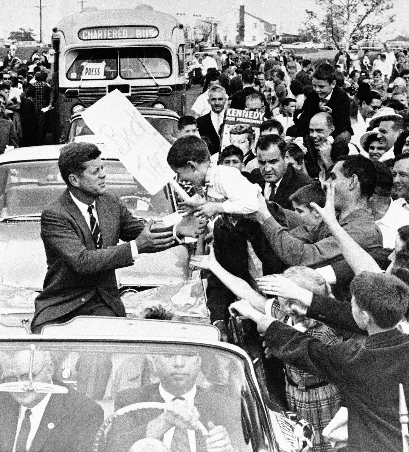 Sen. John F. Kennedy, democratic presidential nominee, reaches out for unidentified youngster held out be enthusiastic father as the senator's motorcade moved through out cheering crowd at Levittown, NJ., Oct. 16, 1960 this afternoon. Kennedy address throng officially estimated at 20,000 in Levittown, shopping plaza. The crowd interrupted Kennedy's speech with applause when he said he had disagreements with Vice President Nixon. (AP Photo) ORG XMIT: APHS256336