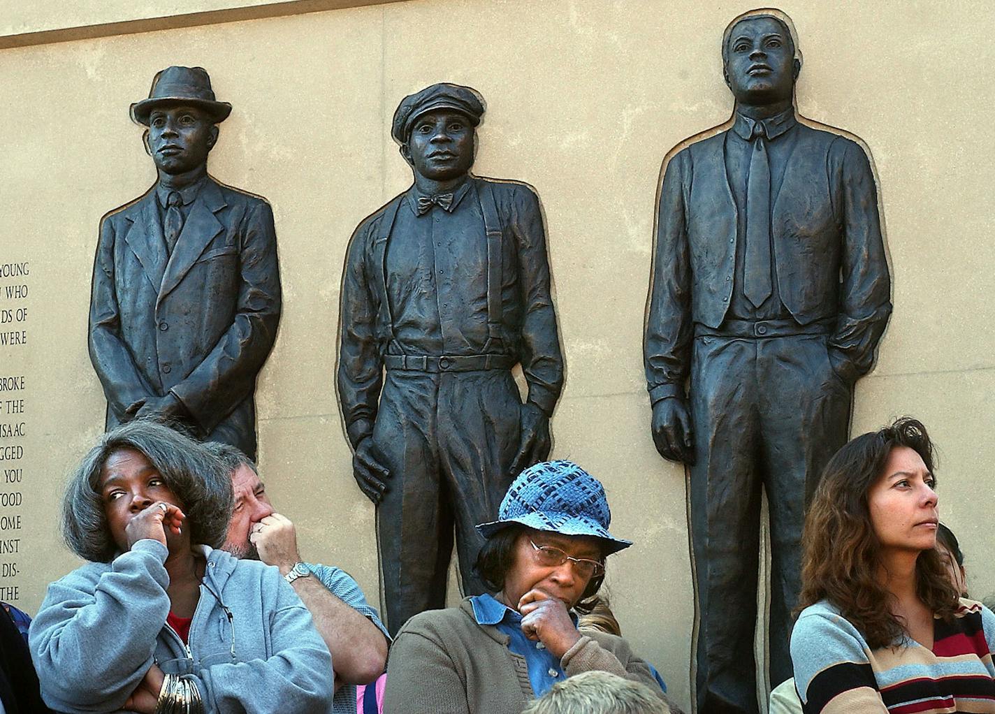 From the left, Elsa Robinson, Lela El Fundi, and Evie Tanner, all of Duluth, reflected during the Clayton Jackson McGhie Lynching Memorial unveiling in 2003. Above them are, from the left, bronze figures of Elias Clayton, Elmer Jackson and Isaac McGhie.