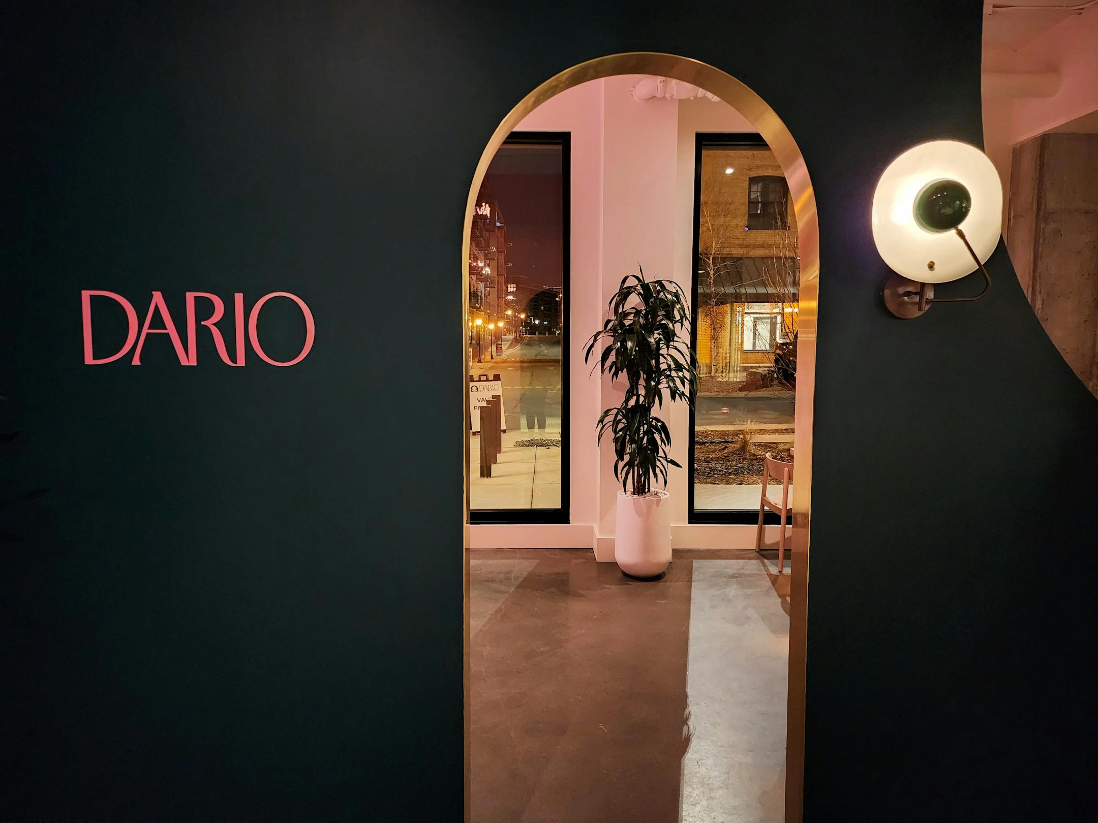 A teal wall that says "Dario" in pink with an opening into a dining room that shows a plant and big picture windows