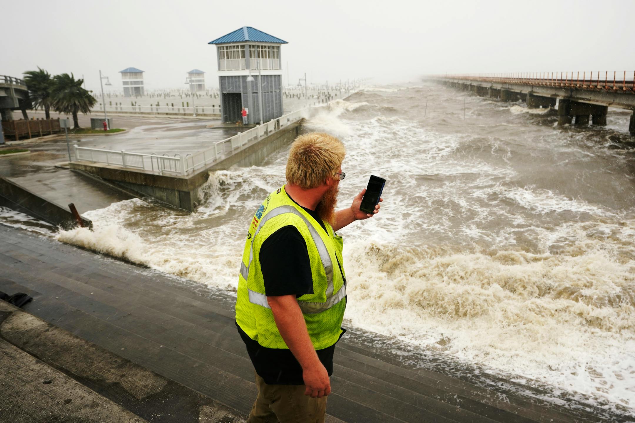 A utility worker photographs waves as they slam against a sea wall at the city marina as outer bands of Hurricane Ida arrive Sunday, Aug. 29, 2021, in Bay Saint Louis, Miss. (AP Photo/Steve Helber)