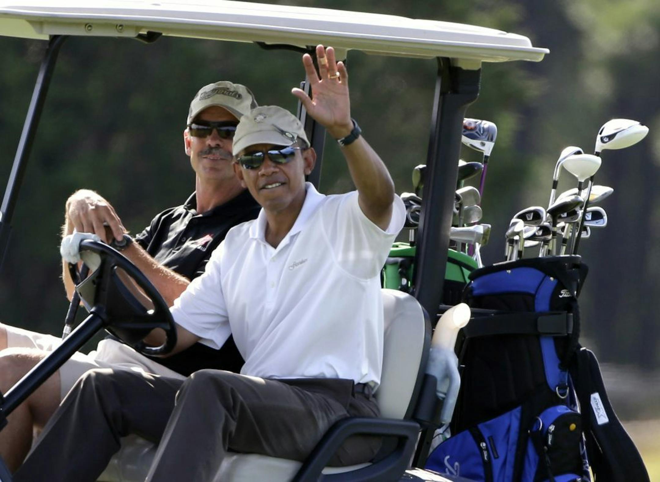 Aug. 17, 2013: President Barack Obama, right, waves to a crowd of onlookers while driving a golf cart with businessman Glenn Hutchins, behind, as they golf on Martha's Vineyard